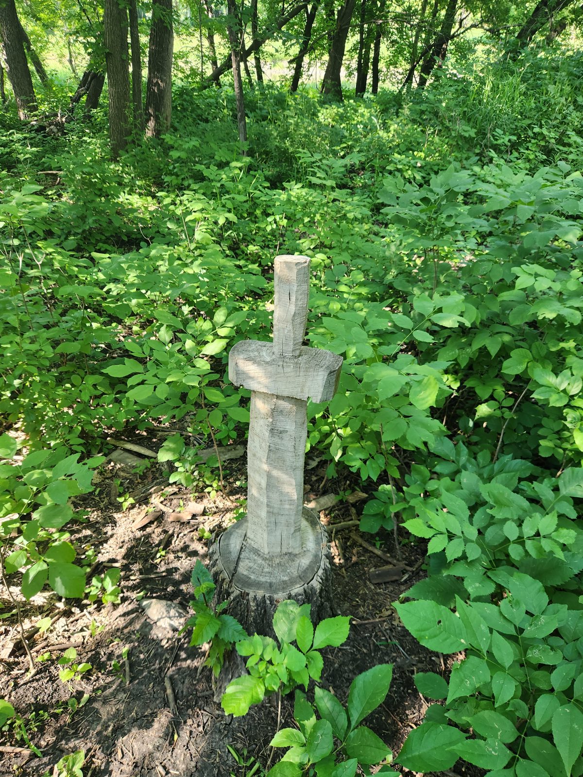 An old tree stump about 4 feet high that has a sword carved out of it with the handle up and the bottom of the sword displaying as "lodged" in the stump